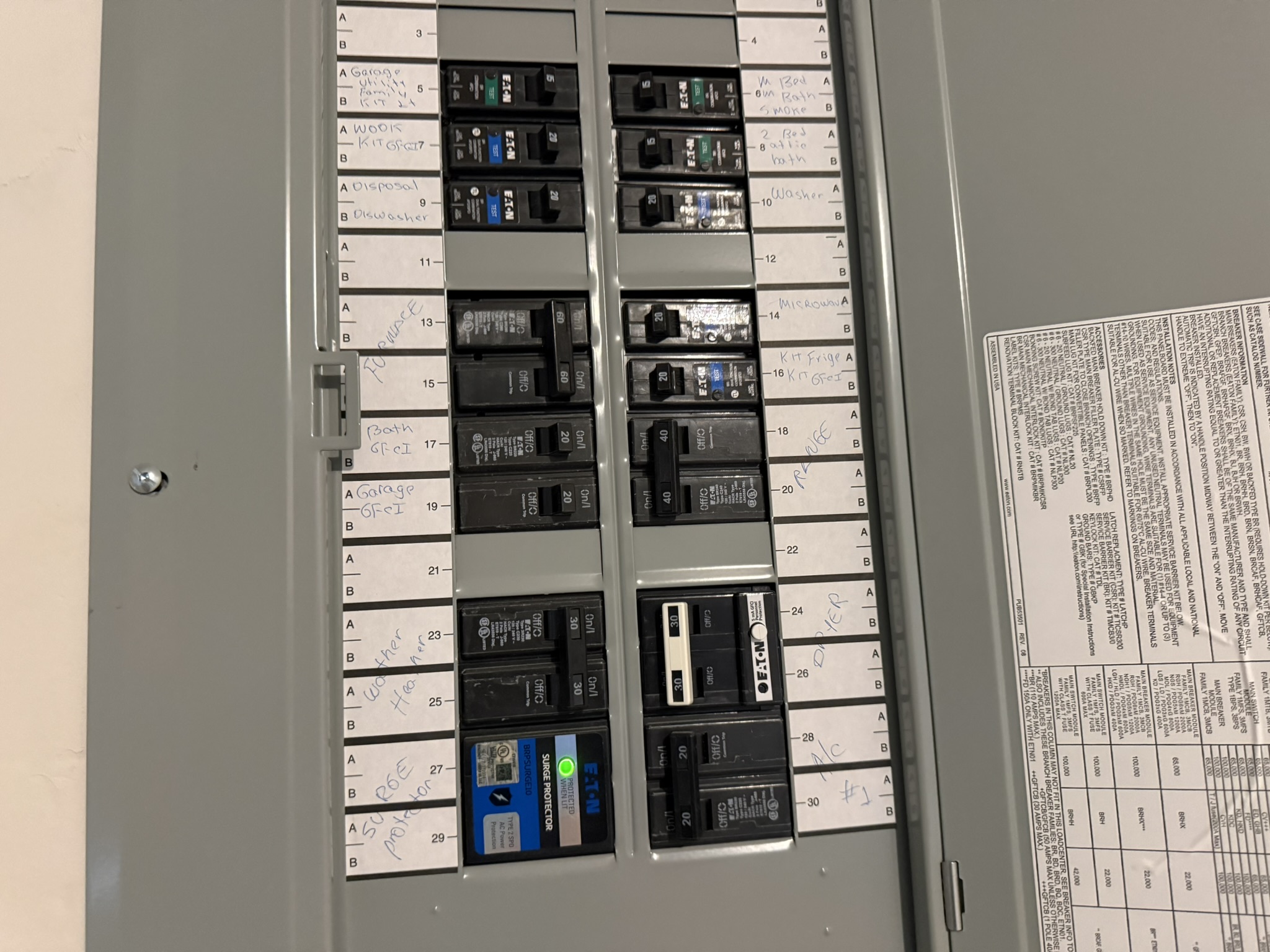 Open gray electrical circuit breaker panel with rows of labeled switches, including a blue breaker with a green indicator light; technical, utilitarian scene.